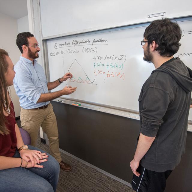 professor teaching two students on a whiteboard