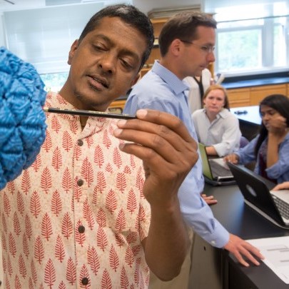 Two professors teach a group of students using a large-scale model of a molecule