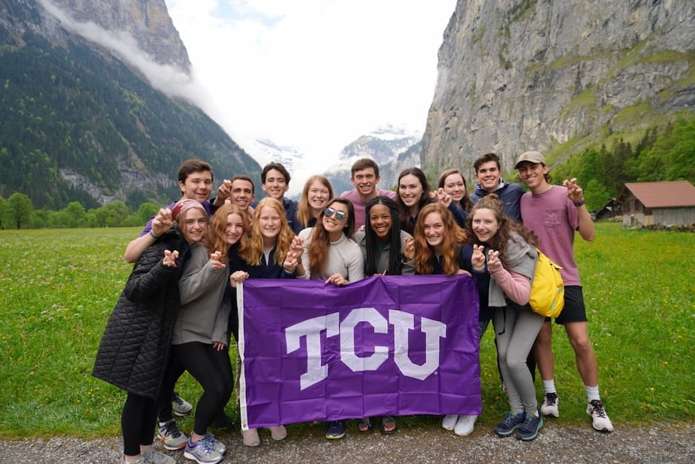 Study abroad students holding up a TCU flag with mountains visible behind them