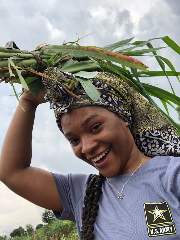 Kayla Thomas smiling and carrying plant stalks in her head