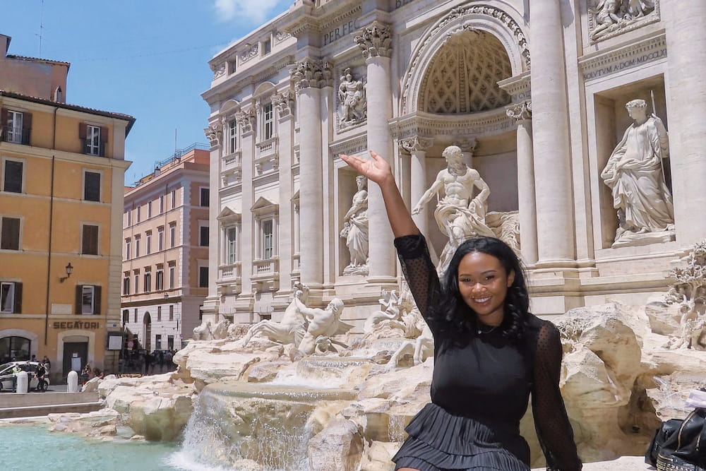 Kennedy posing with her arm up in the air in front of a white building with statues in Italy