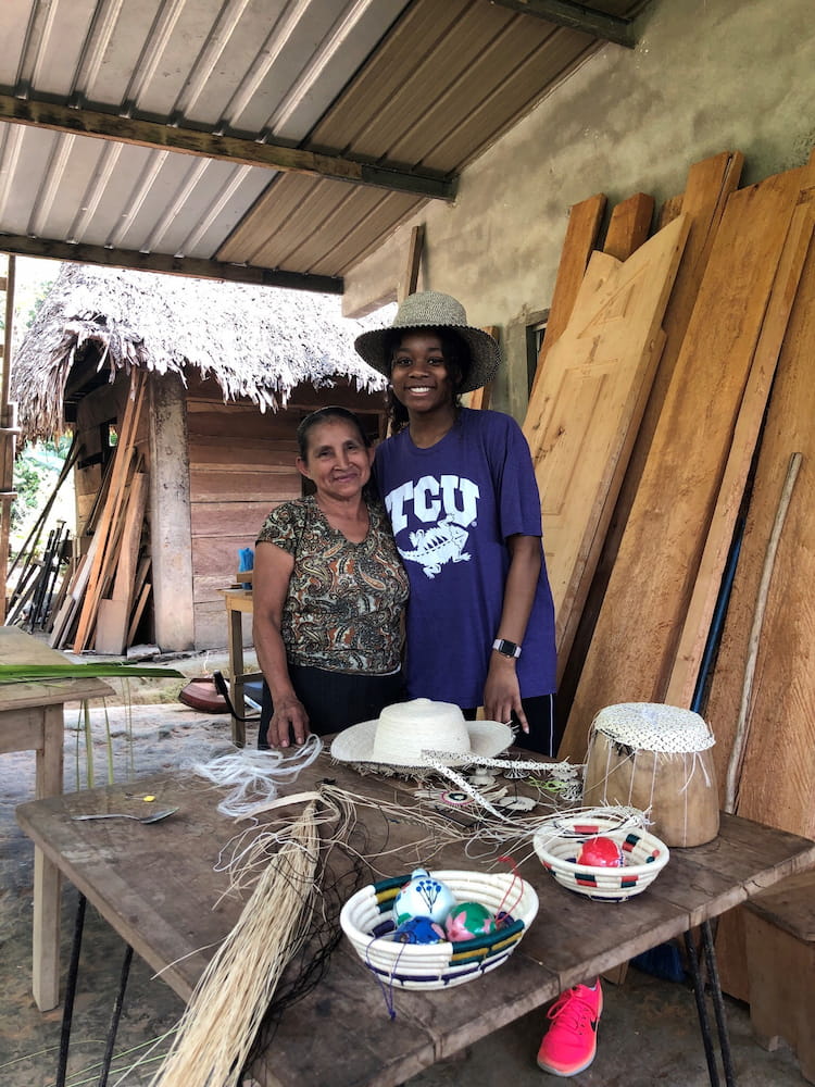Kynnedy Brown wearing a purple TCU shirt and posing with a woman in front of a table with various fiber craft materials