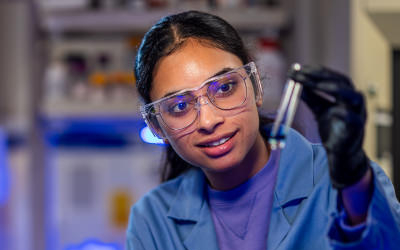A student wearing safety goggles and a lab coat working in a lab