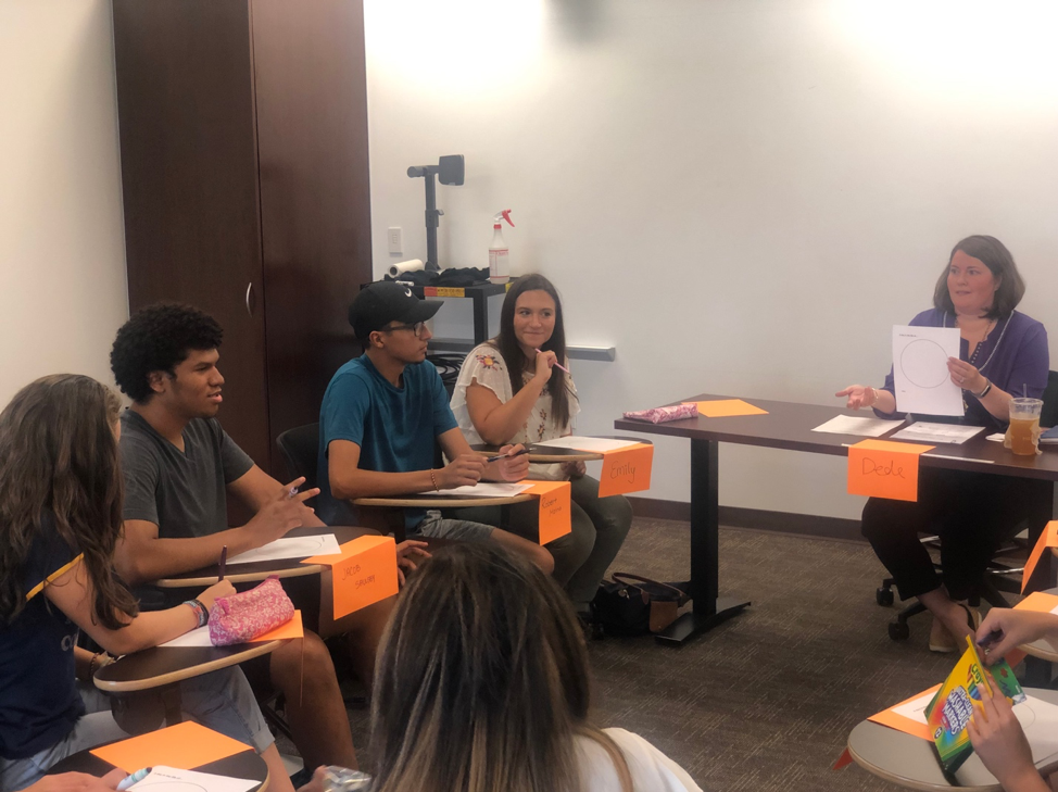 STEM Scholars sitting at desks with large orange signs hanging off the edge of their desks