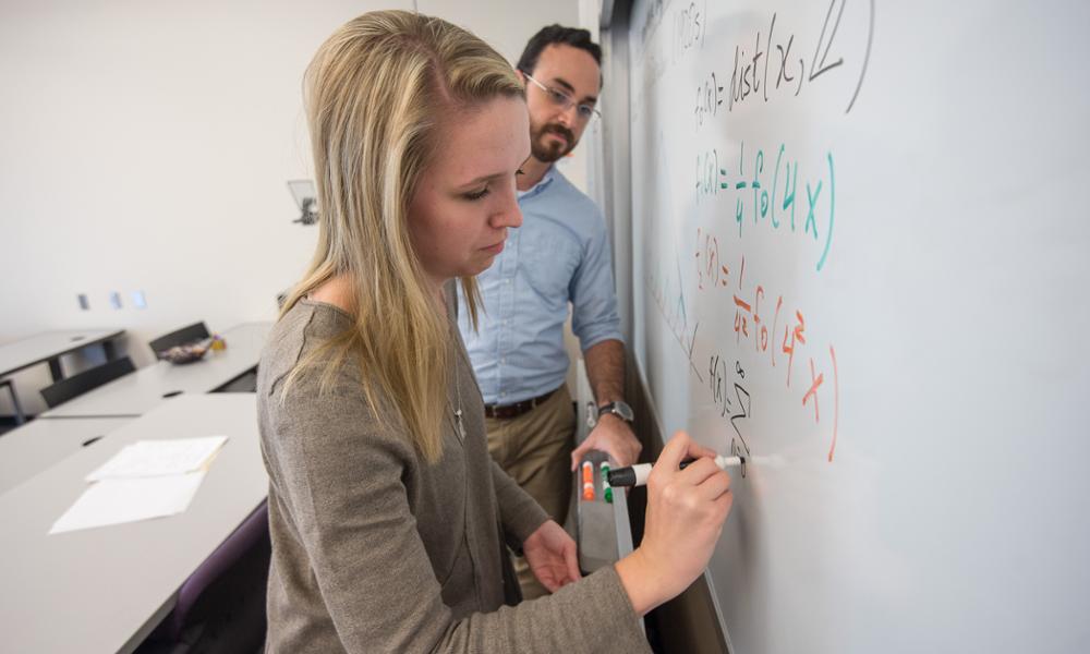 student and professor working on a white board
