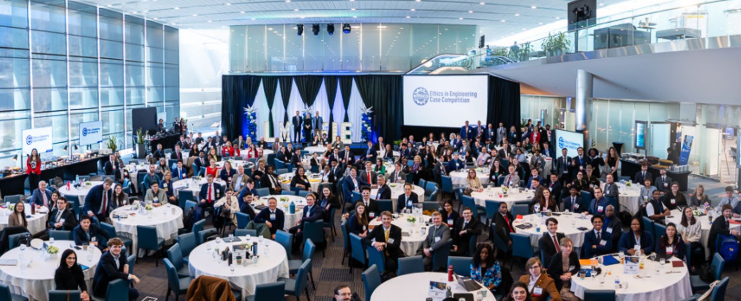 A large conference room filled with attendees seated at round tables covered in blue tablecloths. A stage at the front displays the Detroit Pistons logo and the words "Heads Up" on screens. Attendees appear engaged, with some standing and interacting.