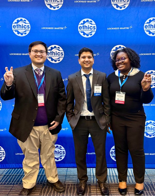 Three people standing in front of a blue backdrop with "Lockheed Martin" and "ethics" logos. They are smiling and displaying Horned Frog hand signs.