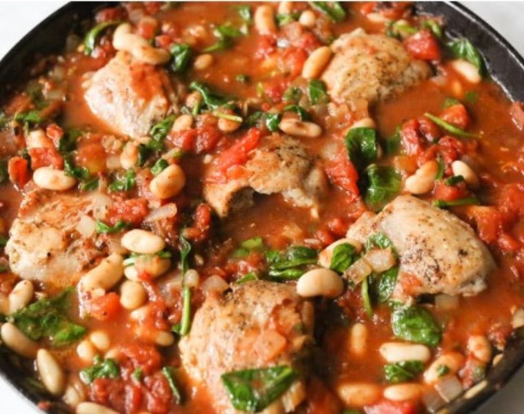Dish with baked chicken, tomatoes, beans and wilted greens.